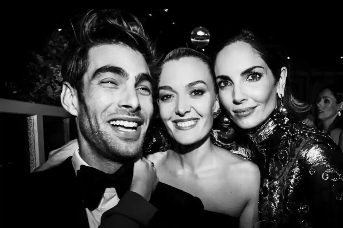Tres personas posan sonrientes para una foto en blanco y negro en un evento elegante. Tres personas posan sonrientes para una foto en blanco y negro en un evento elegante.