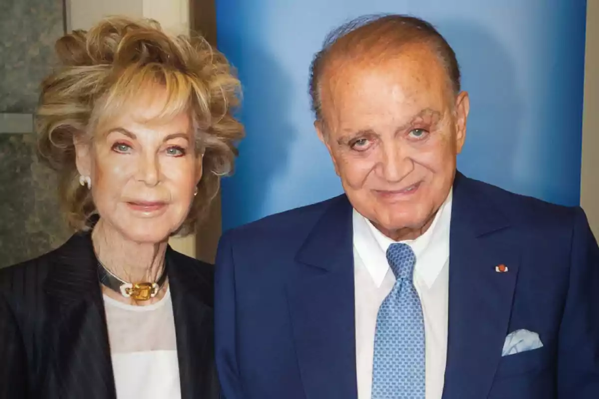 Dos personas mayores posan juntas, ambas vestidas formalmente, con una mujer a la izquierda y un hombre a la derecha, ambos sonriendo frente a un fondo azul. Dos personas mayores posan juntas, ambas vestidas formalmente, con una mujer a la izquierda y un hombre a la derecha, ambos sonriendo frente a un fondo azul.