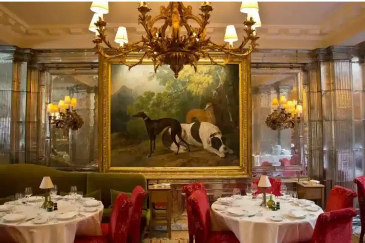 Un elegante comedor con mesas redondas cubiertas de manteles blancos y sillas rojas, decorado con un gran cuadro de perros y un candelabro dorado colgante. Un elegante comedor con mesas redondas cubiertas de manteles blancos y sillas rojas, decorado con un gran cuadro de perros y un candelabro dorado colgante.