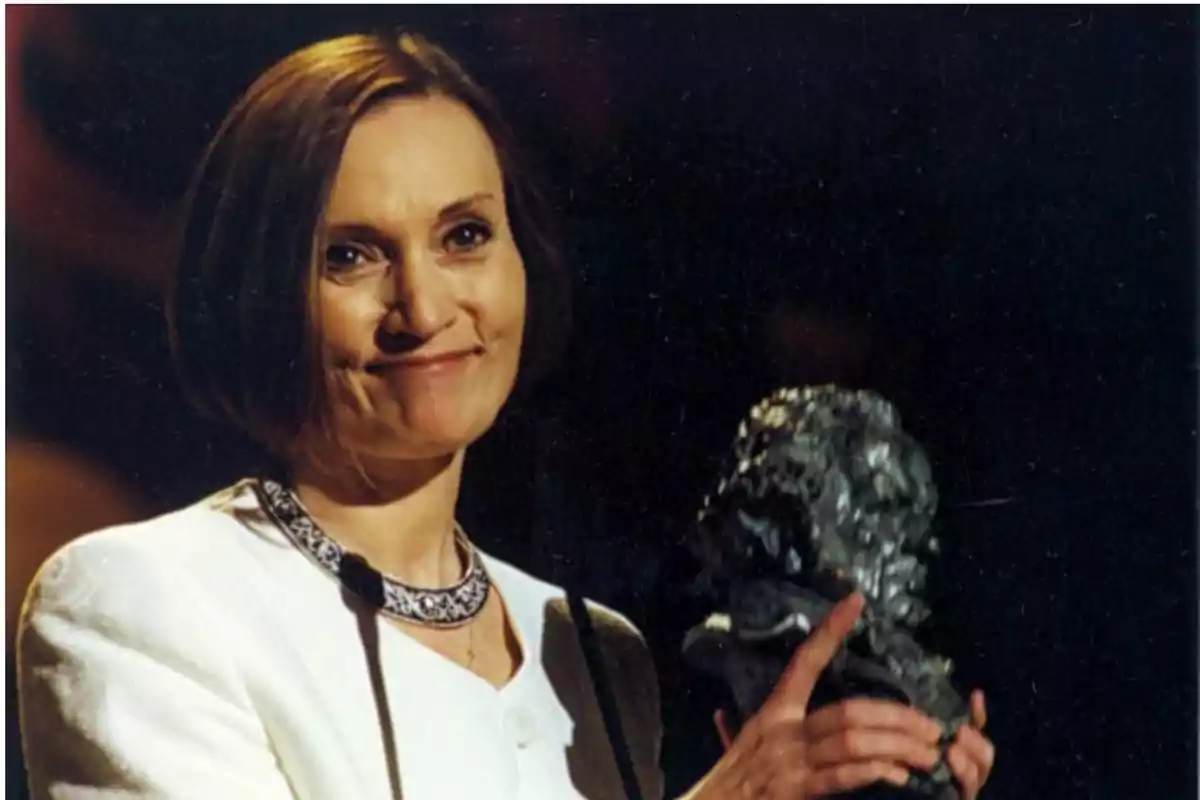Mujer sonriendo con un trofeo en la mano.