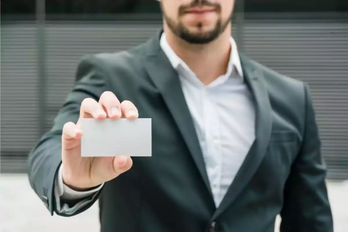 Hombre en traje sosteniendo una tarjeta en blanco frente a él.