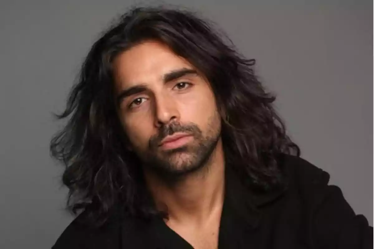 Un hombre con cabello largo y barba ligera mirando a la cámara con expresión neutral. Un hombre con cabello largo y barba ligera mirando a la cámara con expresión neutral.