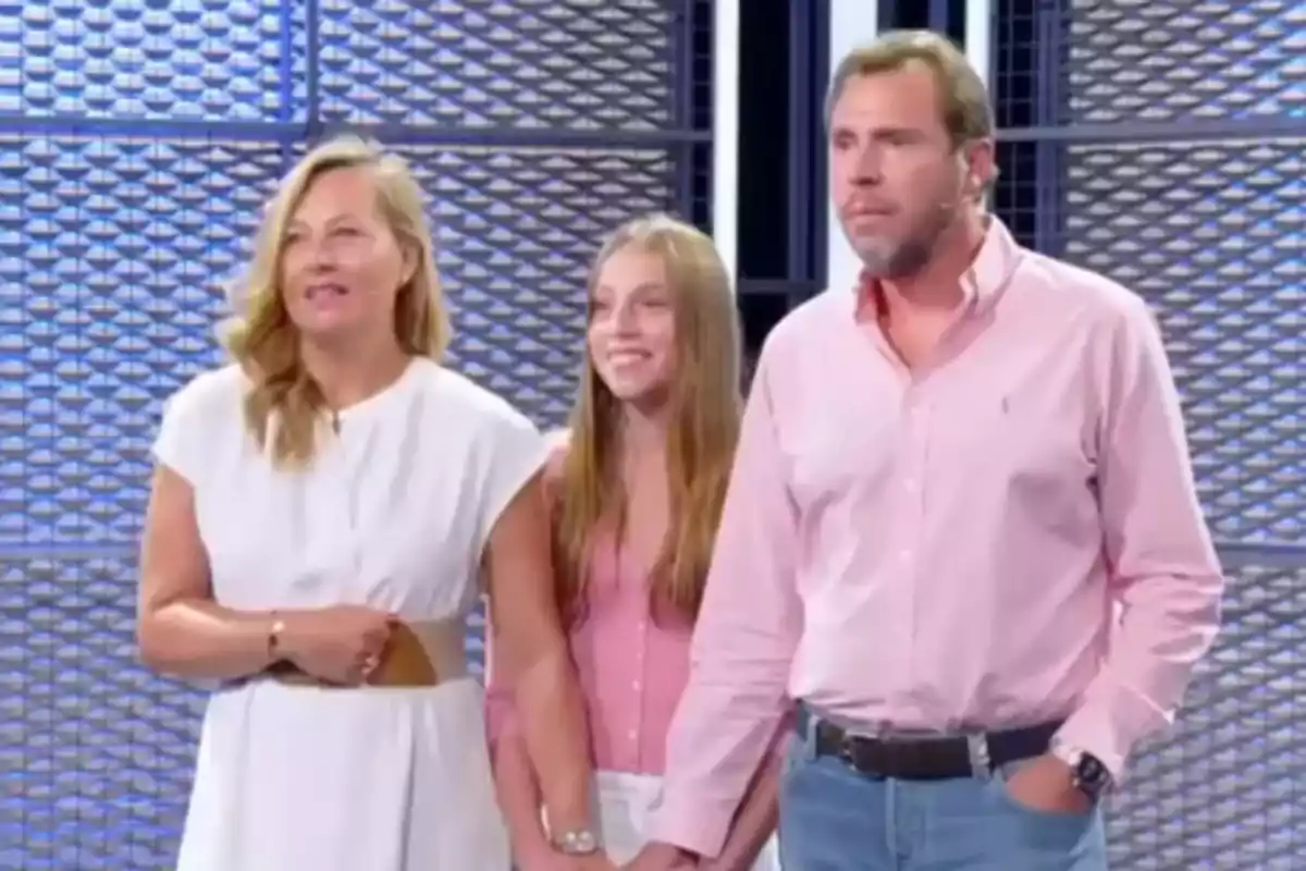 Una familia de tres personas está de pie en un estudio de televisión con un fondo de paneles metálicos. Una familia de tres personas está de pie en un estudio de televisión con un fondo de paneles metálicos.