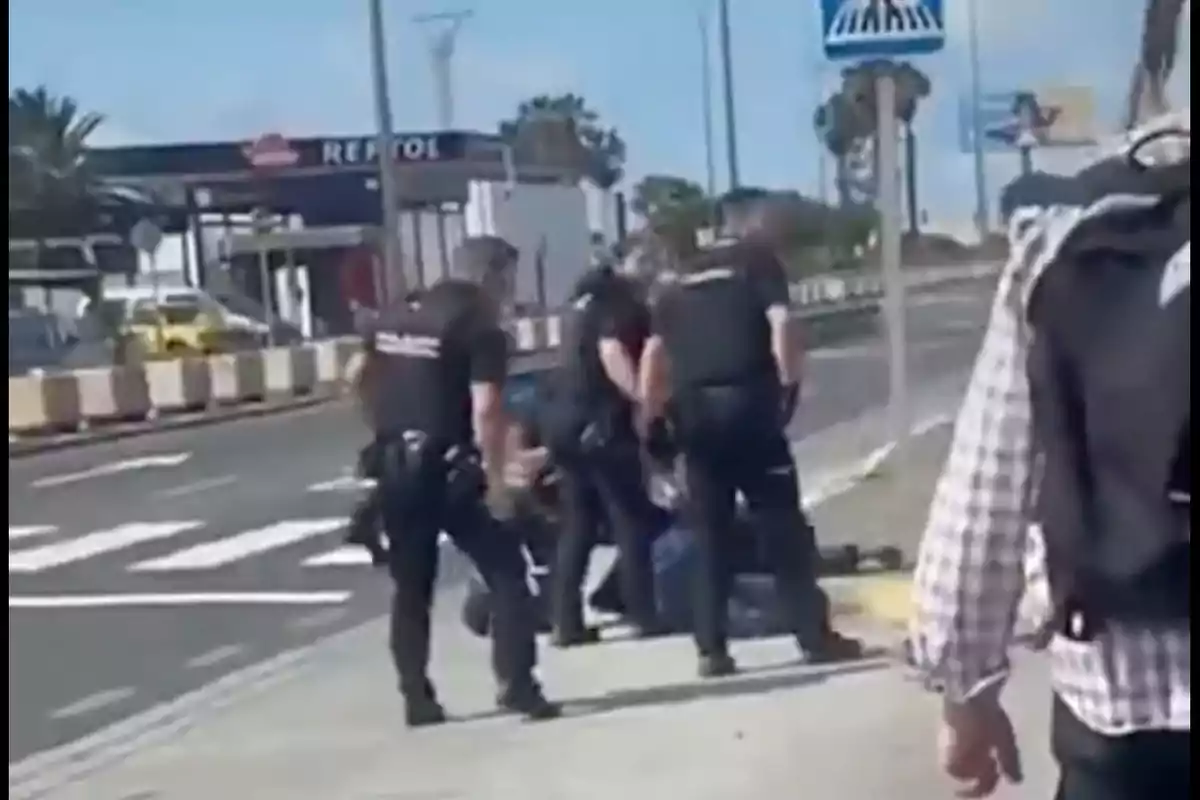 Un grupo de policías detiene a una persona en la acera cerca de una estación de servicio.