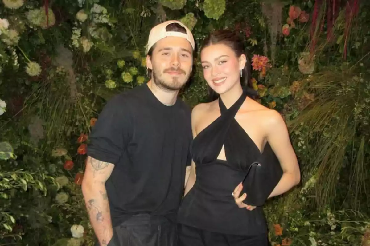 Una pareja posando frente a un fondo de plantas y flores.