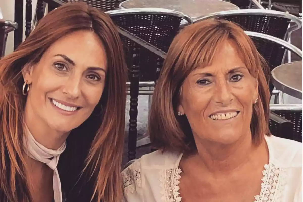 Dos mujeres sonrientes posan juntas en un entorno al aire libre con mesas y sillas de fondo. Dos mujeres sonrientes posan juntas en un entorno al aire libre con mesas y sillas de fondo.