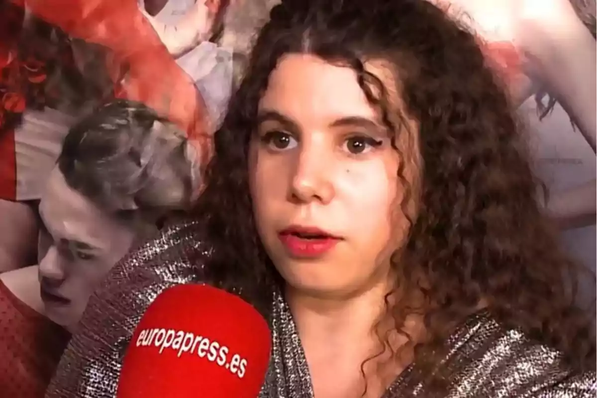 Una persona con cabello rizado y un micrófono rojo de europapress.es está siendo entrevistada frente a un fondo con imágenes borrosas. Una persona con cabello rizado y un micrófono rojo de europapress.es está siendo entrevistada frente a un fondo con imágenes borrosas.