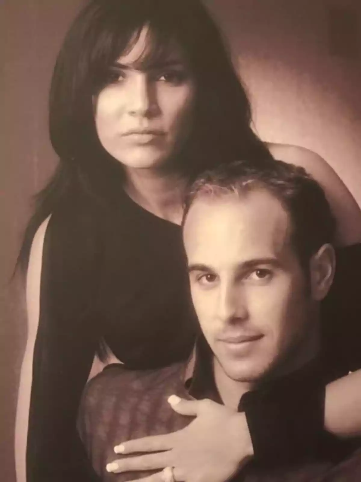 Una pareja posando para una fotografía en blanco y negro, donde la mujer está detrás del hombre con su brazo sobre su hombro. Una pareja posando para una fotografía en blanco y negro, donde la mujer está detrás del hombre con su brazo sobre su hombro.