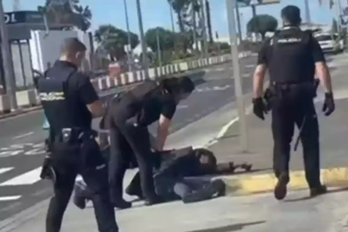 Un grupo de policías detiene a una persona en el suelo en una acera durante el día.