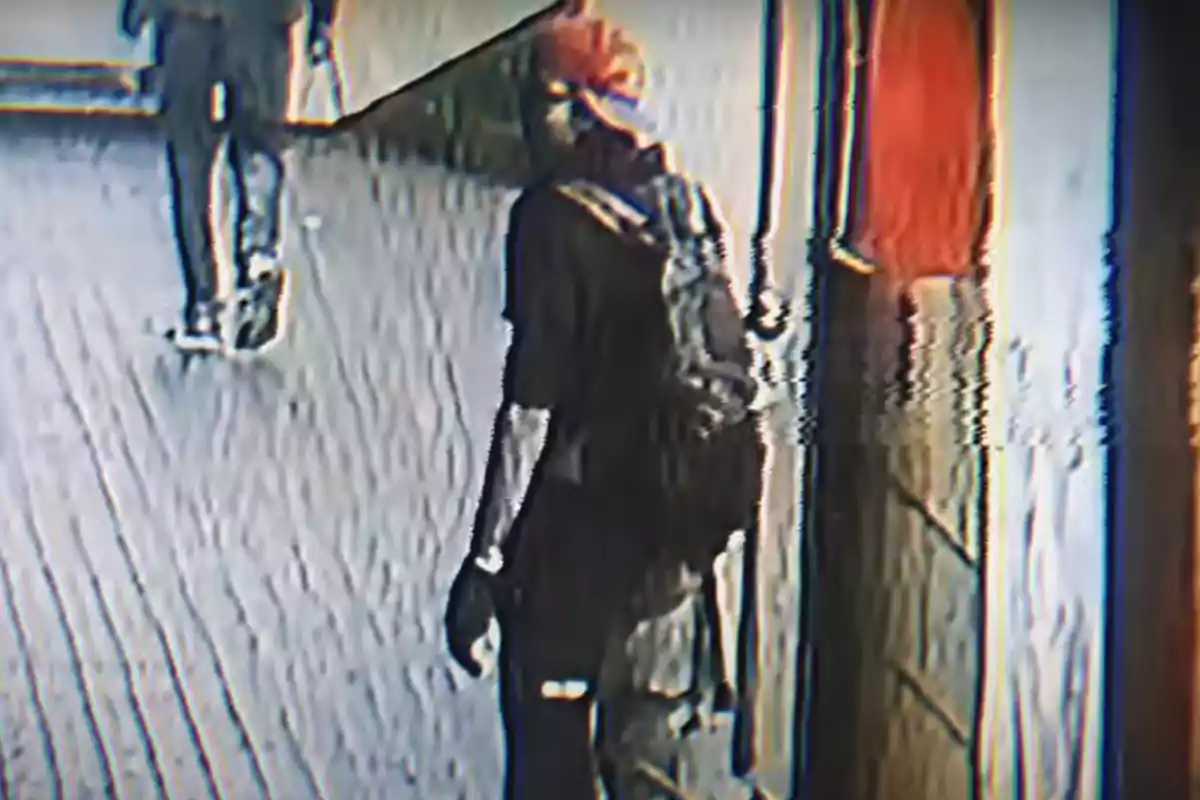 Una persona con gorra y mochila camina por un pasillo mientras otra persona se aleja en el fondo. Una persona con gorra y mochila camina por un pasillo mientras otra persona se aleja en el fondo.