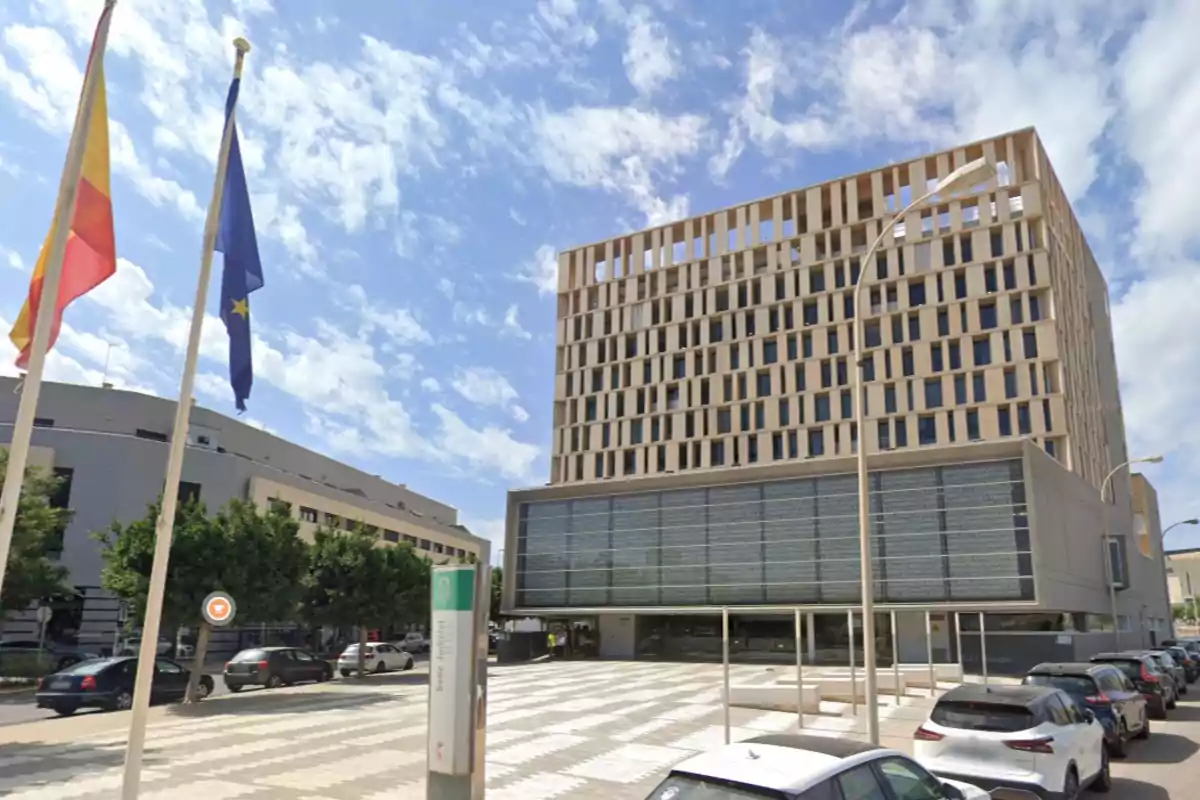 Edificio moderno con fachada de diseño geométrico junto a una calle con coches aparcados y dos banderas ondeando en un día soleado. Edificio moderno con fachada de diseño geométrico junto a una calle con coches aparcados y dos banderas ondeando en un día soleado.