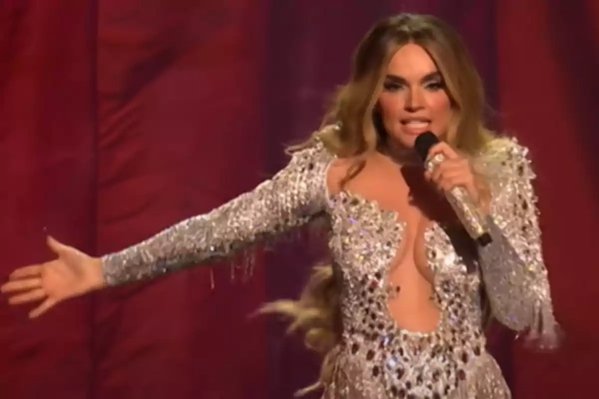 Cantante con vestido brillante y micrófono en mano actuando en un escenario con fondo rojo.