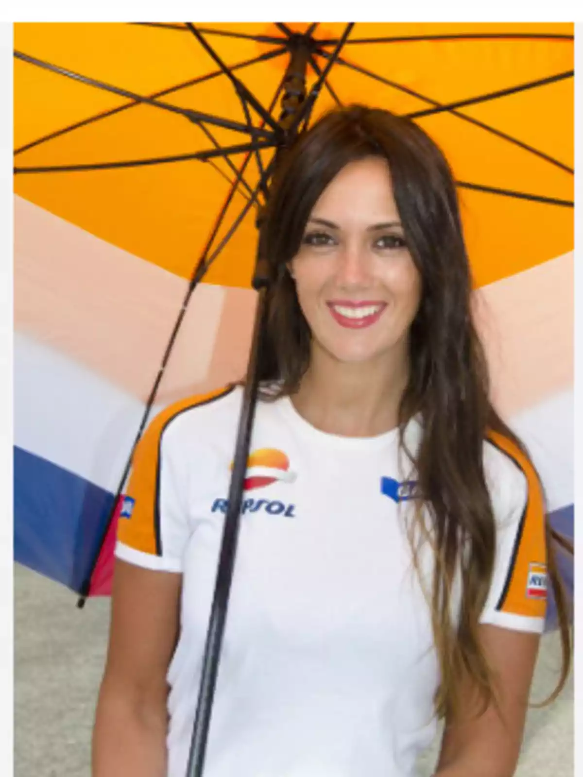 Mujer sonriente con camiseta de Repsol sosteniendo un paraguas amarillo Mujer sonriente con camiseta de Repsol sosteniendo un paraguas amarillo