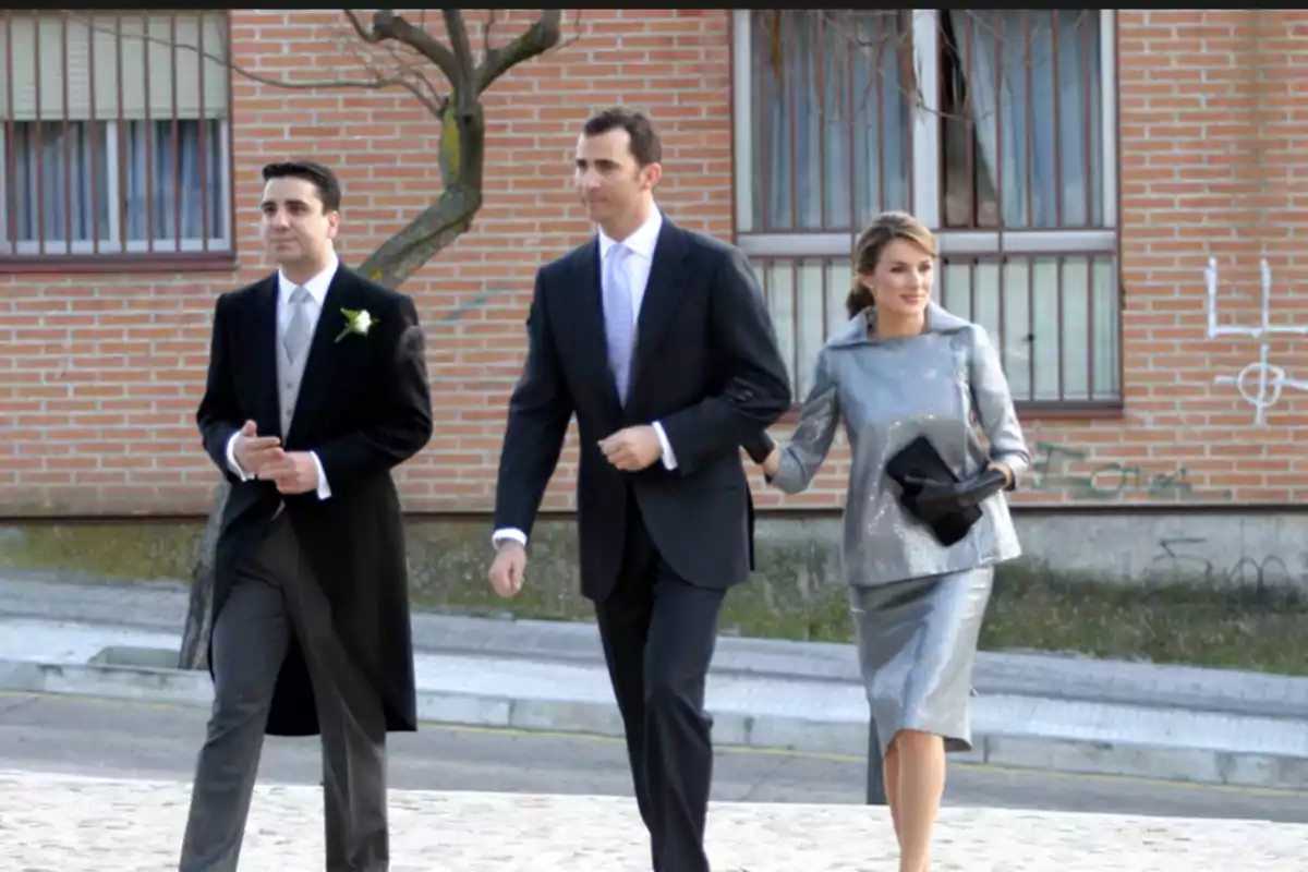 Tres personas elegantemente vestidas caminan por la acera frente a un edificio de ladrillo Tres personas elegantemente vestidas caminan por la acera frente a un edificio de ladrillo
