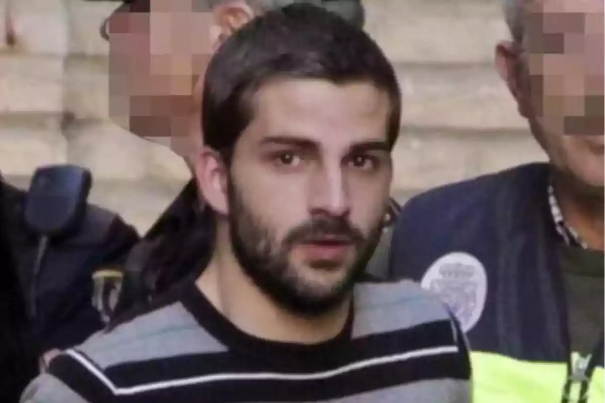 Un hombre de barba y cabello corto es escoltado por personas con el rostro pixelado. Un hombre de barba y cabello corto es escoltado por personas con el rostro pixelado.