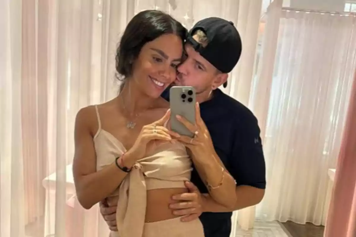 Pareja abrazada tomándose una selfie frente a un espejo con cortinas de fondo Pareja abrazada tomándose una selfie frente a un espejo con cortinas de fondo