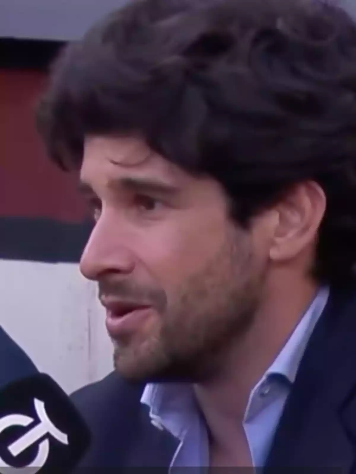 Hombre de cabello oscuro y barba corta hablando frente a un micrófono durante una entrevista Hombre de cabello oscuro y barba corta hablando frente a un micrófono durante una entrevista