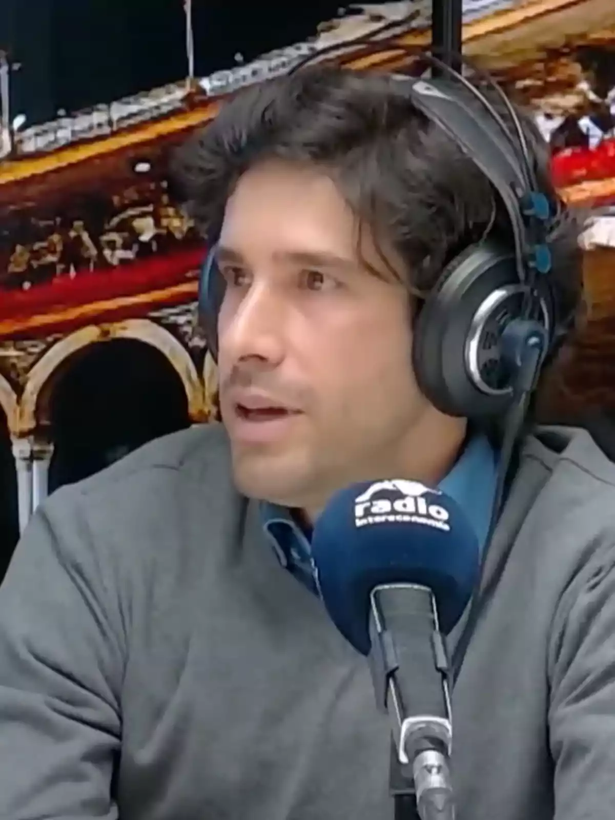 Hombre con auriculares hablando frente a un micrófono azul en un estudio de radio Hombre con auriculares hablando frente a un micrófono azul en un estudio de radio