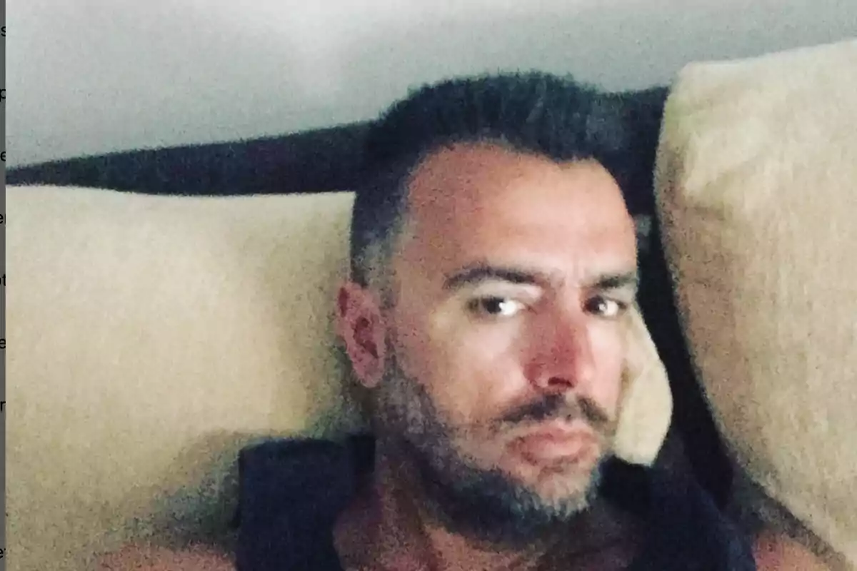 Hombre recostado sobre almohadas mirando hacia la cámara con expresión seria Hombre recostado sobre almohadas mirando hacia la cámara con expresión seria