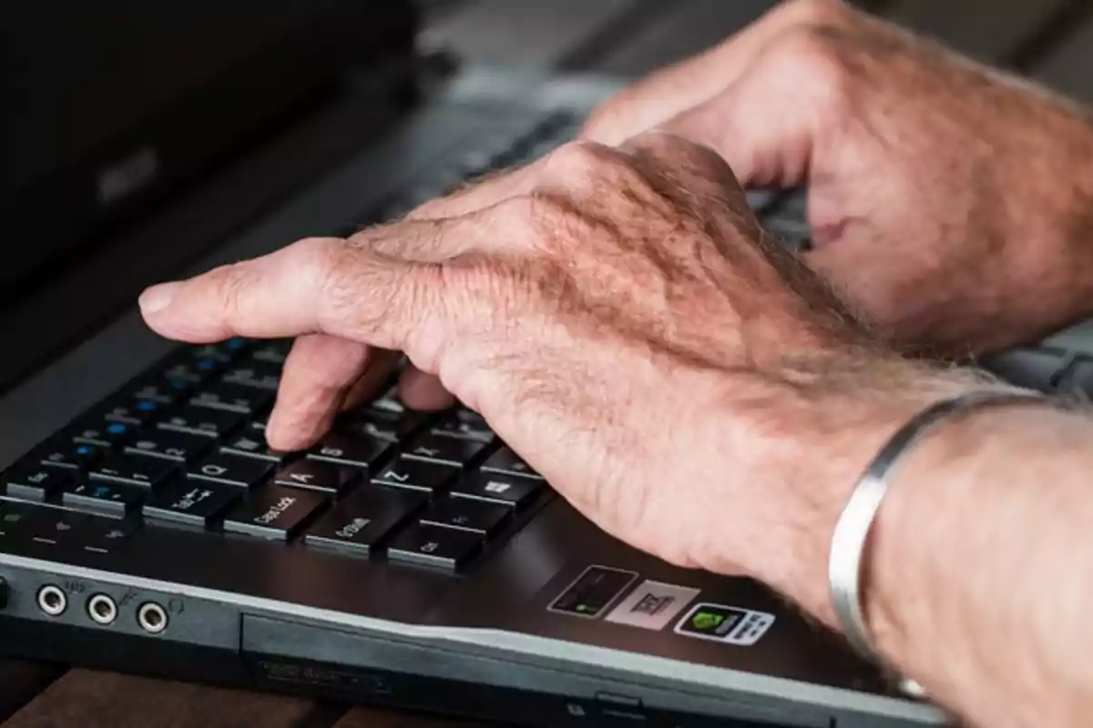 Manos de una persona mayor escribiendo en el teclado de una computadora portátil