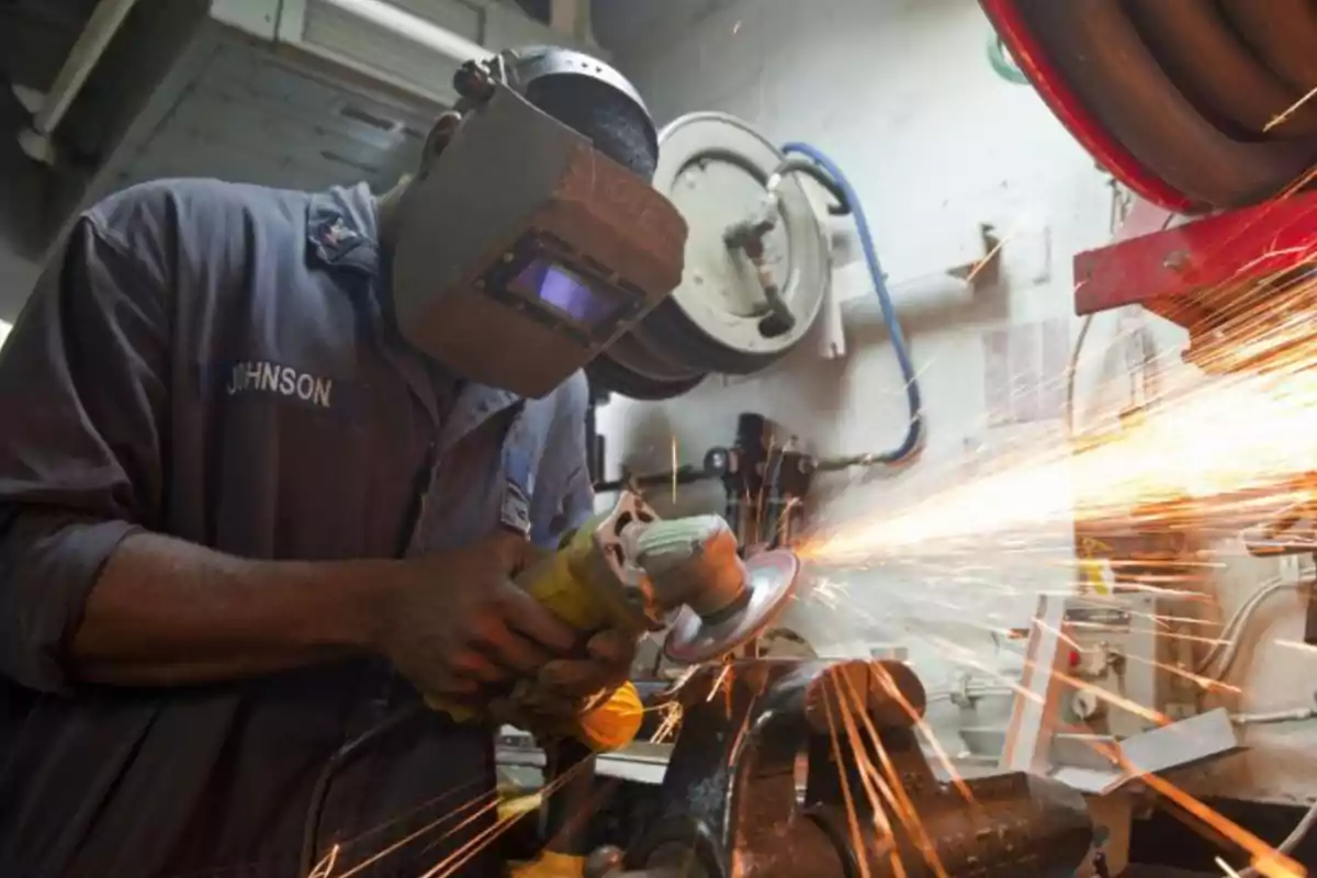 Persona usando careta de protección mientras trabaja con una herramienta eléctrica que genera chispas en un taller industrial
