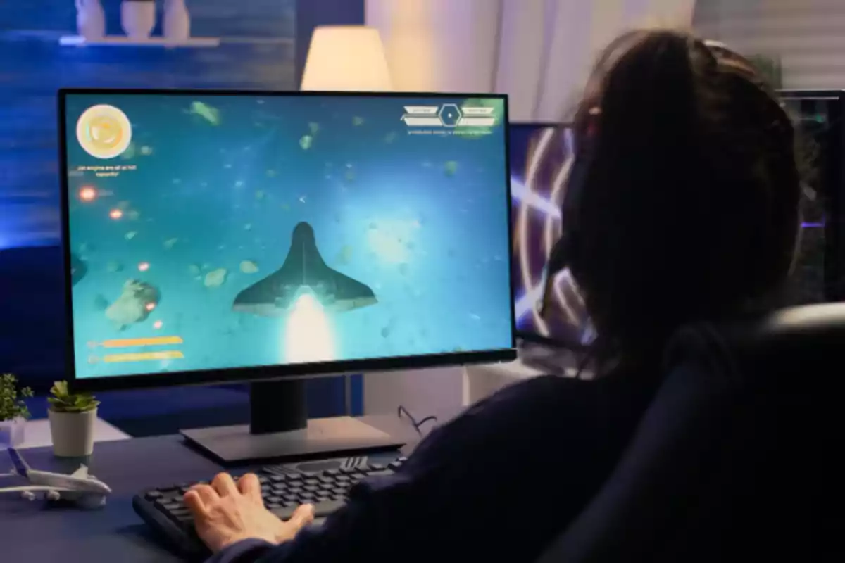 Persona jugando un videojuego espacial en una computadora con teclado y auriculares en un ambiente iluminado