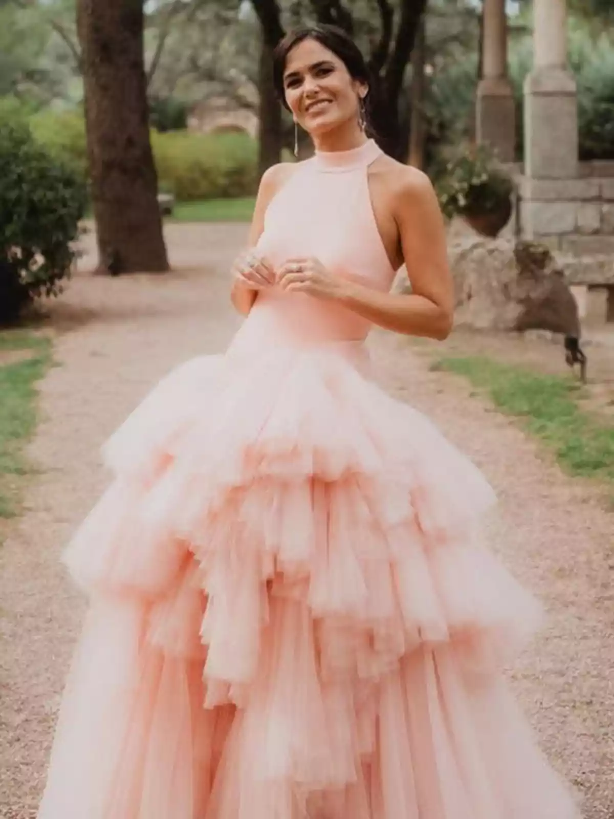Mujer sonriente con vestido de tul rosa claro en un jardín Mujer sonriente con vestido de tul rosa claro en un jardín