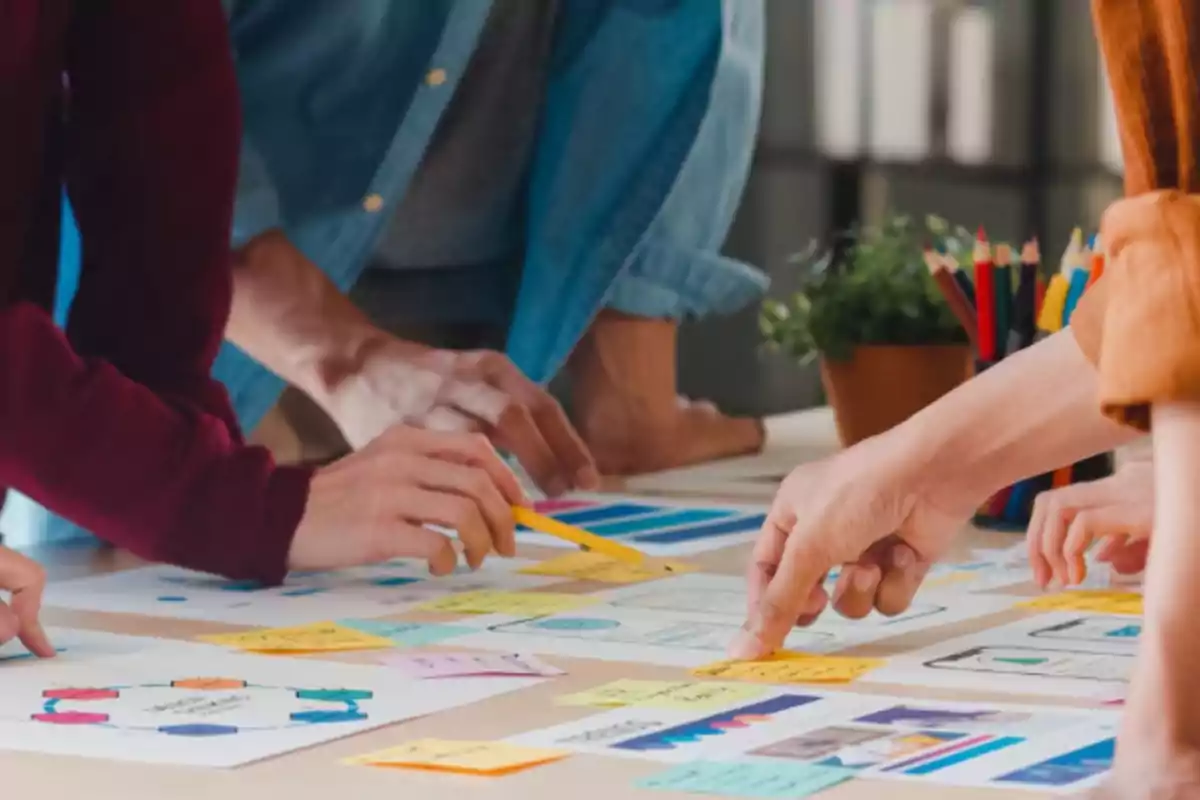 Personas colaborando en una mesa con papeles, gráficos y notas adhesivas de colores