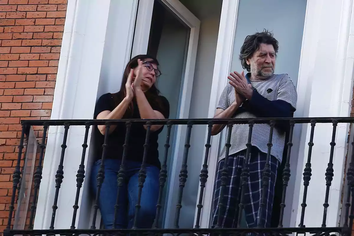 Dos personas aplauden de pie en un balcón de un edificio Dos personas aplauden de pie en un balcón de un edificio