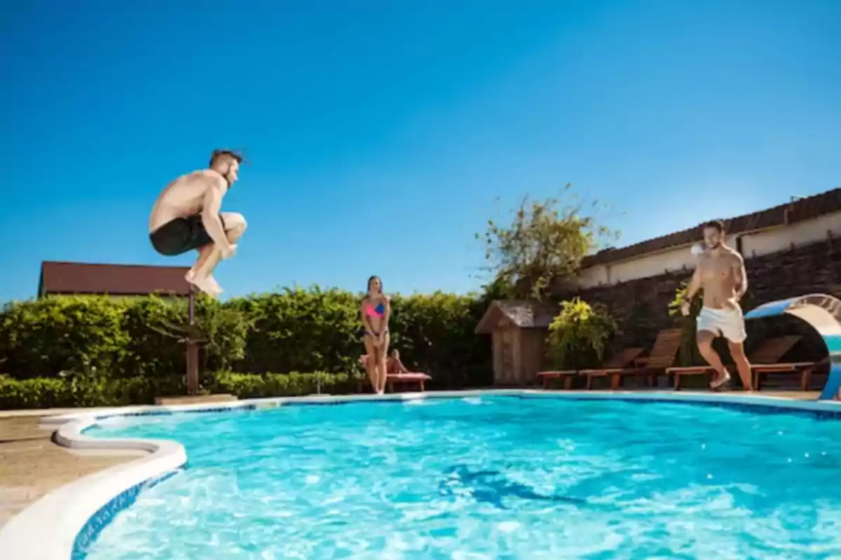 Tres personas disfrutan de un día soleado en una piscina, dos hombres saltan al agua mientras una mujer observa desde el borde