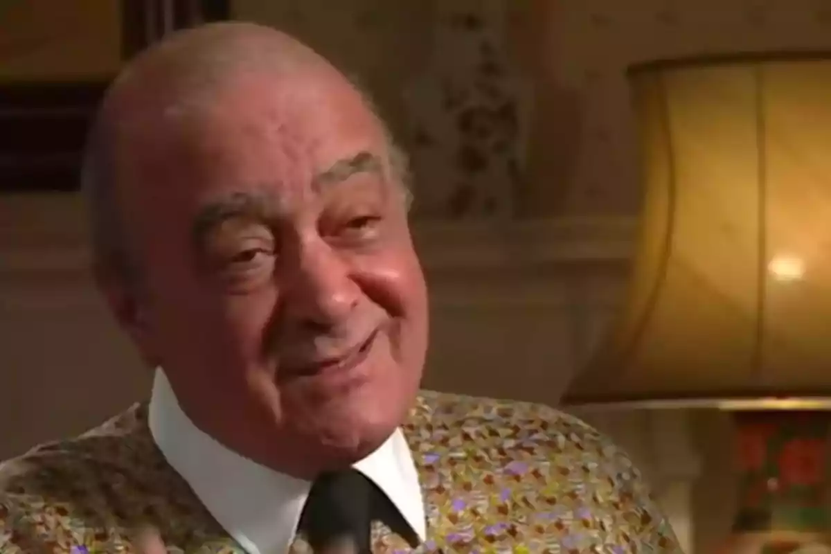 Hombre mayor calvo sonriendo mientras habla en una habitación iluminada con una lámpara al fondo Hombre mayor calvo sonriendo mientras habla en una habitación iluminada con una lámpara al fondo