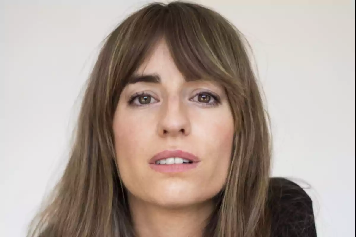 Retrato de una mujer de cabello castaño largo y lacio con flequillo mirando al frente sobre un fondo claro