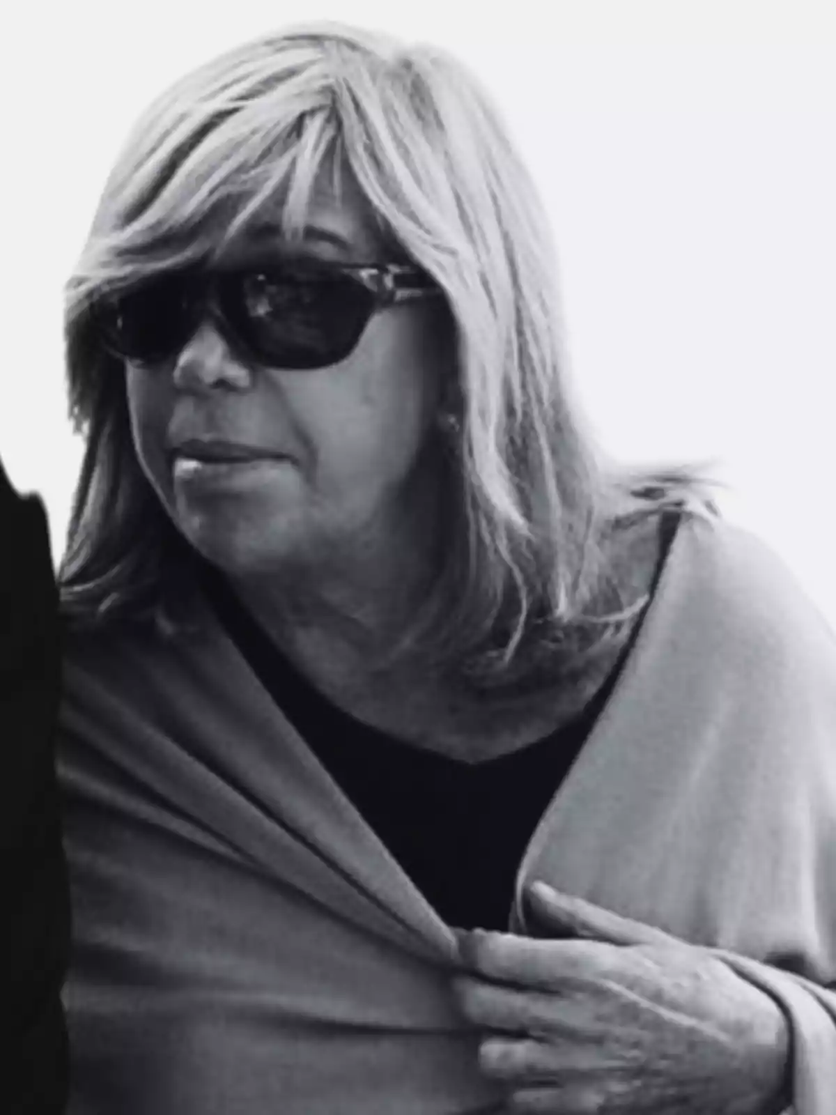 Mujer de cabello rubio y gafas oscuras mirando hacia un lado mientras sostiene su abrigo Mujer de cabello rubio y gafas oscuras mirando hacia un lado mientras sostiene su abrigo