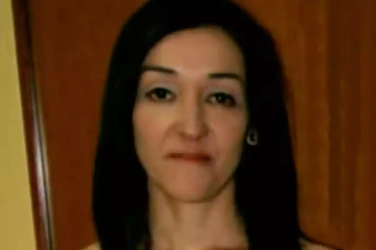 Mujer de cabello oscuro y lacio frente a una puerta de madera con expresión seria