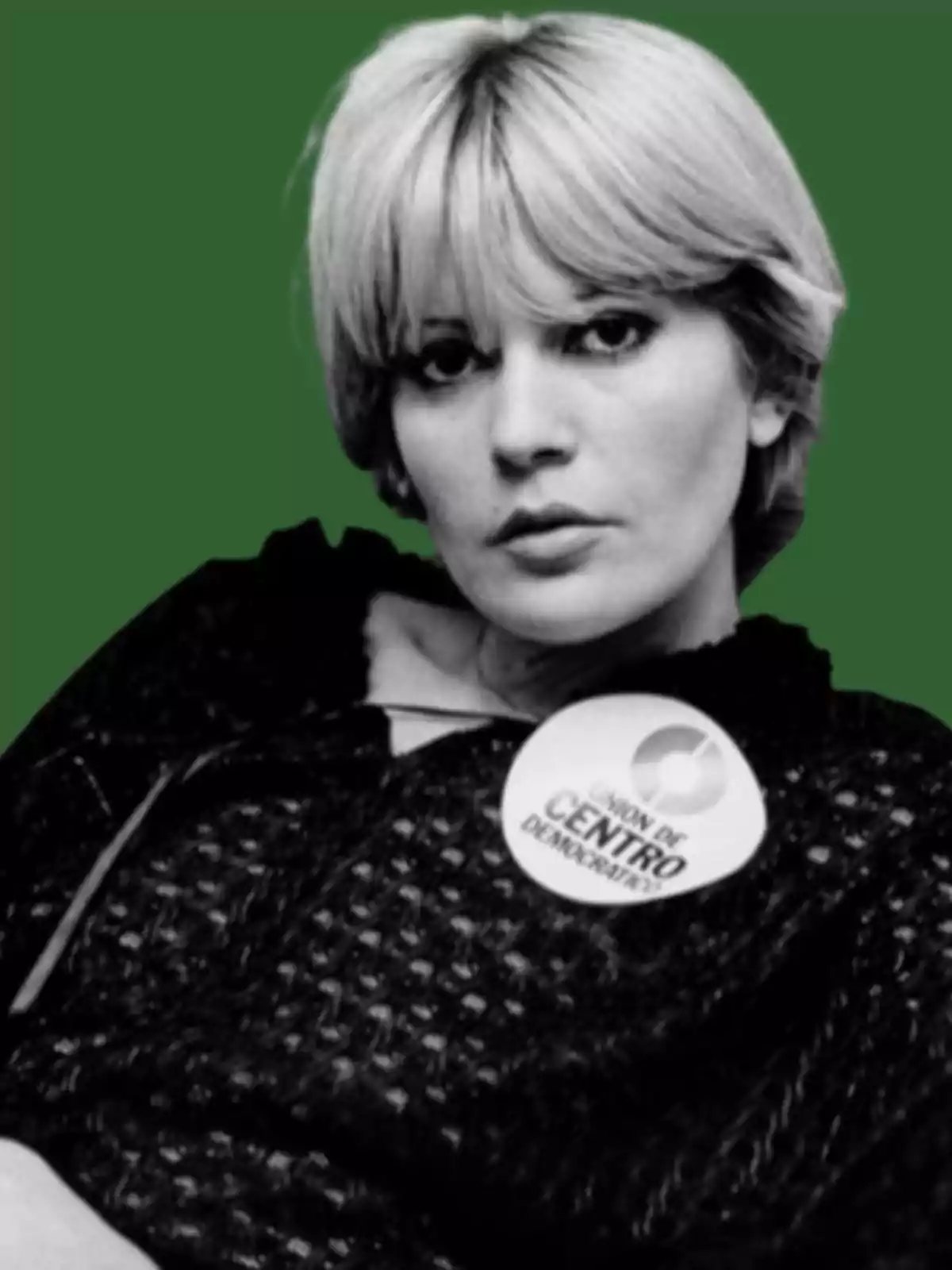 Mujer de cabello corto y rubio con expresión seria, lleva un pin que dice Unión de Centro Democrático sobre su ropa oscura y el fondo es verde Mujer de cabello corto y rubio con expresión seria, lleva un pin que dice Unión de Centro Democrático sobre su ropa oscura y el fondo es verde