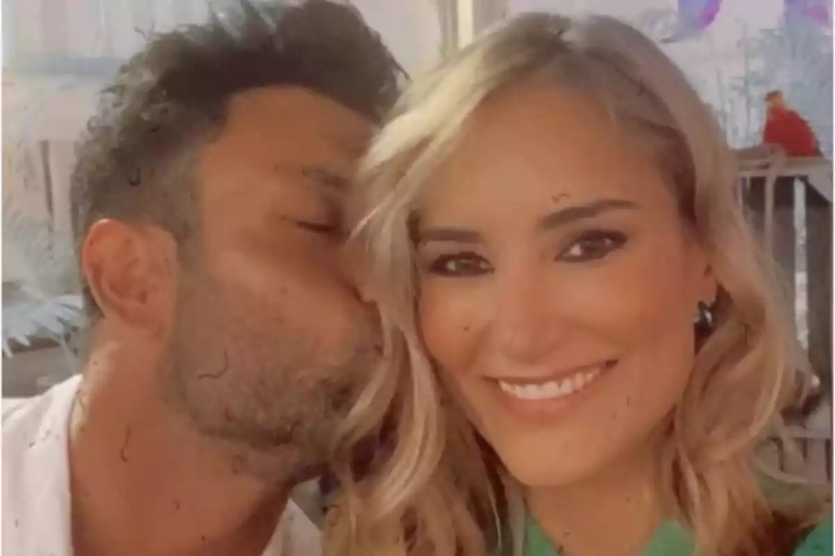 Pareja sonriente mientras el hombre besa en la mejilla a la mujer