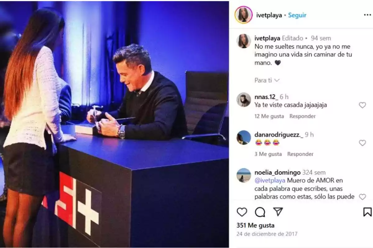 Una mujer joven se encuentra de pie frente a un hombre que está sentado en una mesa firmando un libro, ambos sonríen en un ambiente iluminado con luces azules Una mujer joven se encuentra de pie frente a un hombre que está sentado en una mesa firmando un libro, ambos sonríen en un ambiente iluminado con luces azules