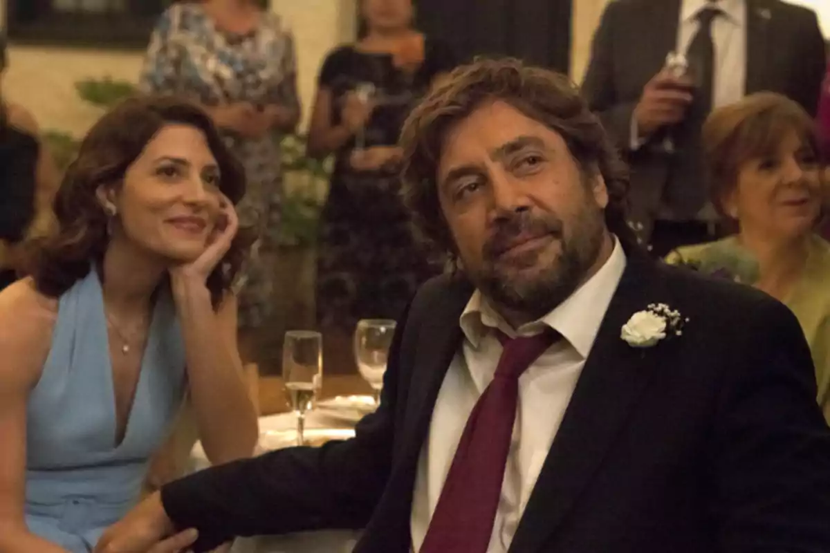 Una pareja elegantemente vestida está sentada en una mesa durante una celebración, rodeada de otras personas en un ambiente festivo. Una pareja elegantemente vestida está sentada en una mesa durante una celebración, rodeada de otras personas en un ambiente festivo.