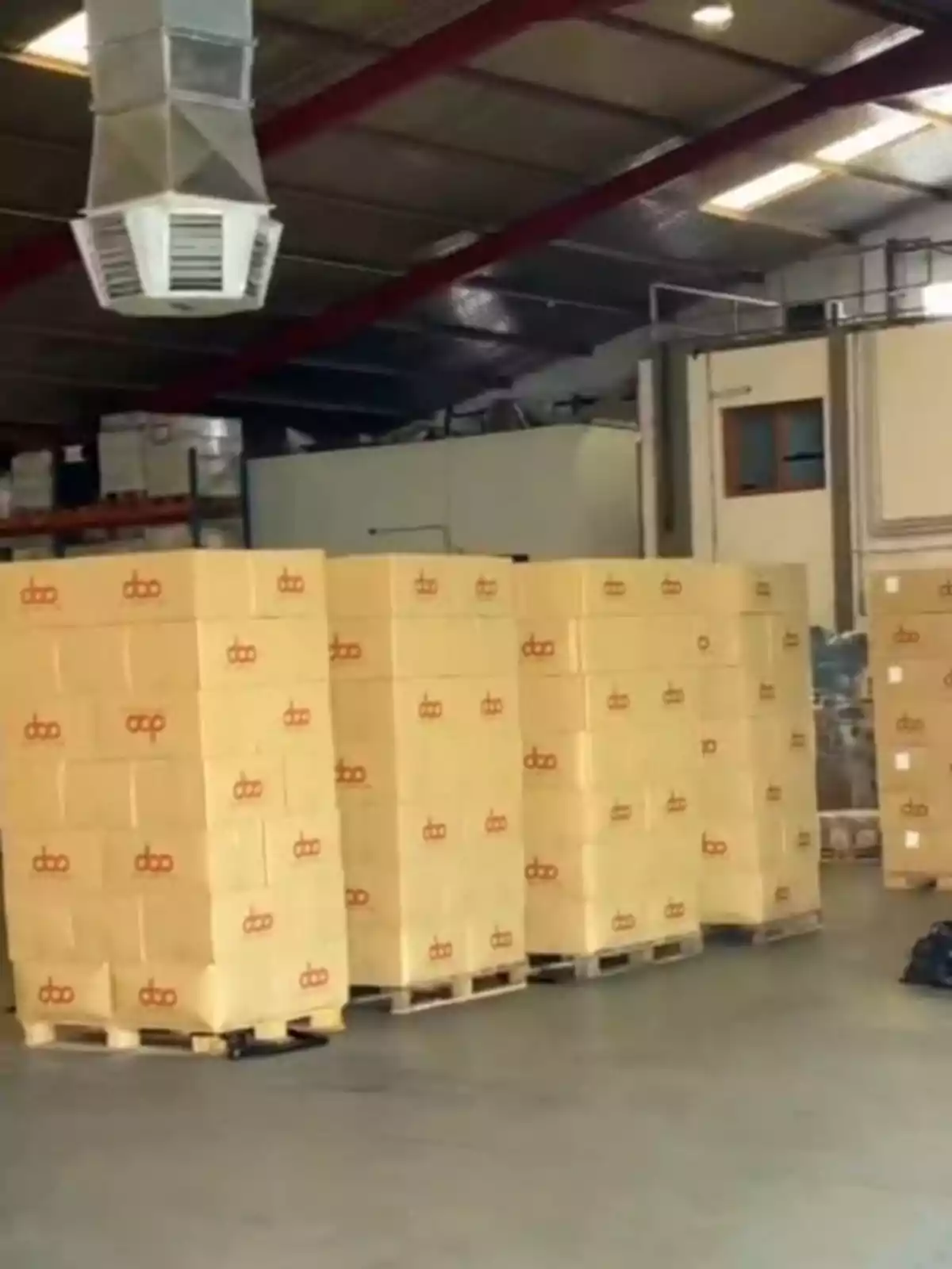 Almacén con cajas apiladas sobre palets y un sistema de ventilación en el techo.