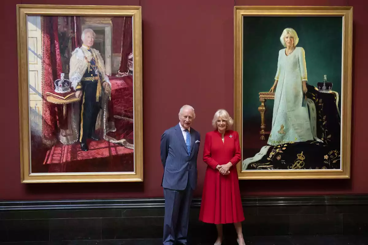 Carlos III y la reina Camila posa frente a dos retratos enmarcados que representan a un hombre y una mujer vestidos con atuendos formales y elegantes. Carlos III y la reina Camila posa frente a dos retratos enmarcados que representan a un hombre y una mujer vestidos con atuendos formales y elegantes.