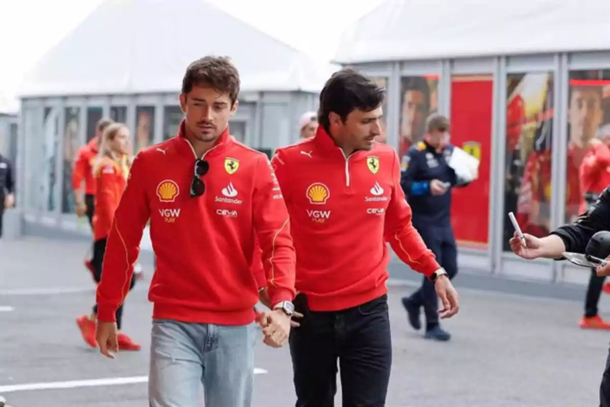 Dos personas con sudaderas rojas de Ferrari caminando en un área de paddock.