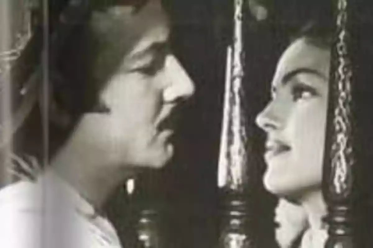Una pareja se mira a través de una reja en una escena en blanco y negro.