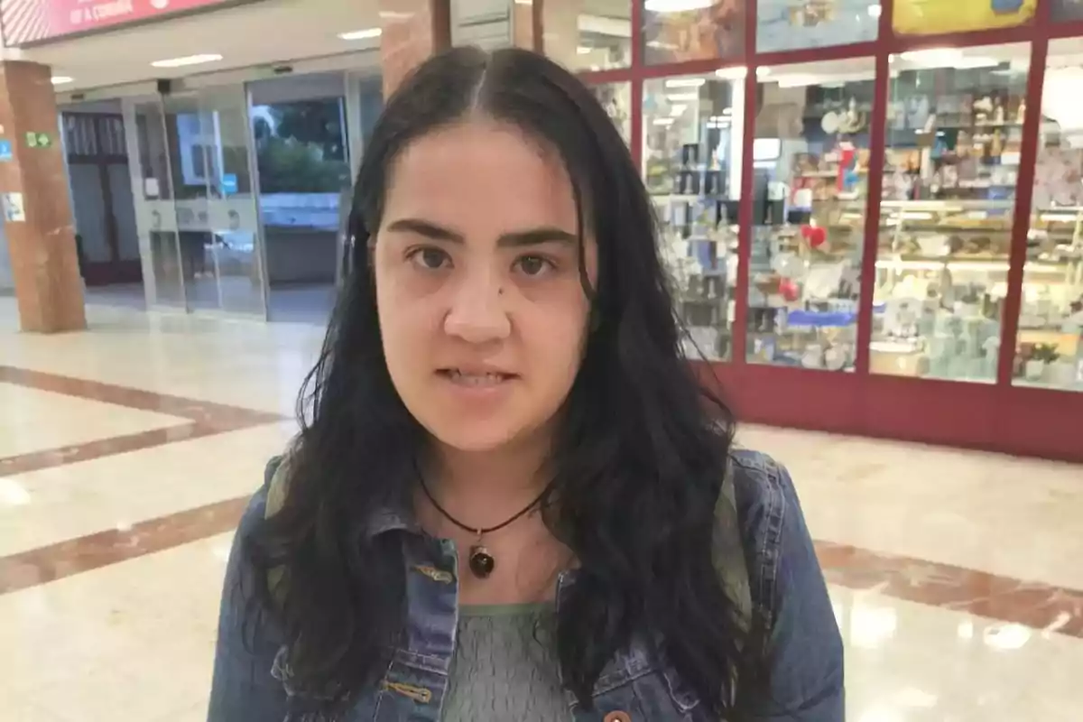 Una persona con cabello oscuro y chaqueta de mezclilla está en el interior de un centro comercial.