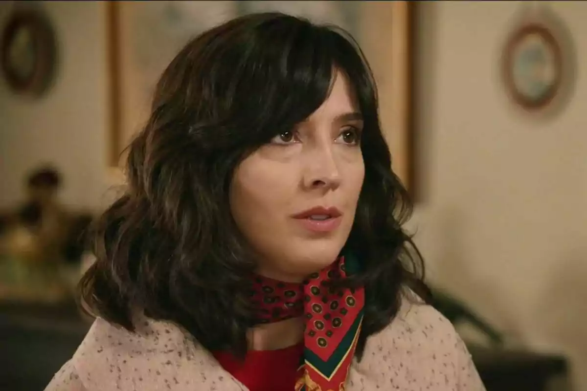 Carolina Lapausa con cabello oscuro y bufanda roja con diseño, mirando hacia arriba en un entorno interior actuando en una escena de 'Sueños de Libertad'. Carolina Lapausa con cabello oscuro y bufanda roja con diseño, mirando hacia arriba en un entorno interior actuando en una escena de 'Sueños de Libertad'.