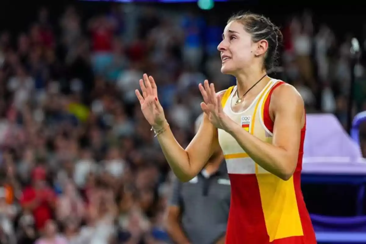 Una atleta emocionada con uniforme de España levanta las manos en un estadio lleno de espectadores.