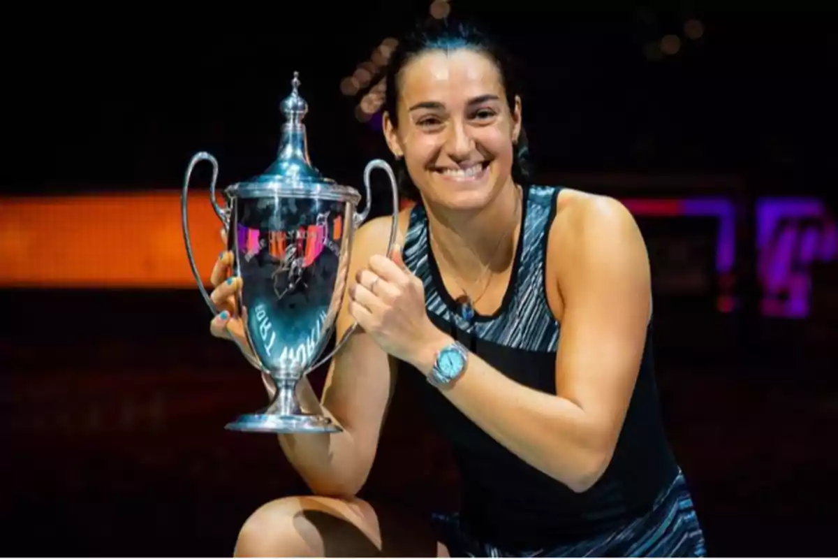 Una persona sonriente sostiene un trofeo plateado en un ambiente iluminado.