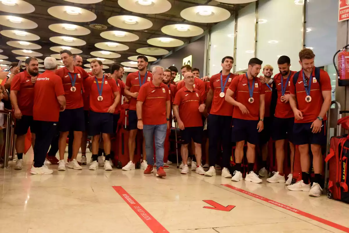 Un grupo de personas con camisetas rojas y medallas se encuentran en un aeropuerto.