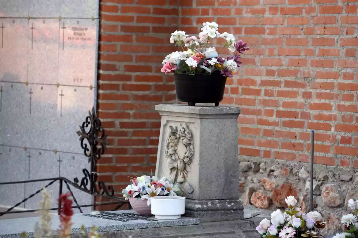 Una tumba adornada con flores en un cementerio, con una pared de ladrillo al fondo.