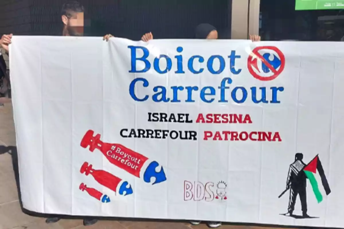 Personas sostienen una pancarta que dice "Boicot Carrefour" con mensajes críticos hacia Israel y Carrefour, acompañada de ilustraciones de bombas y una figura con una bandera palestina.