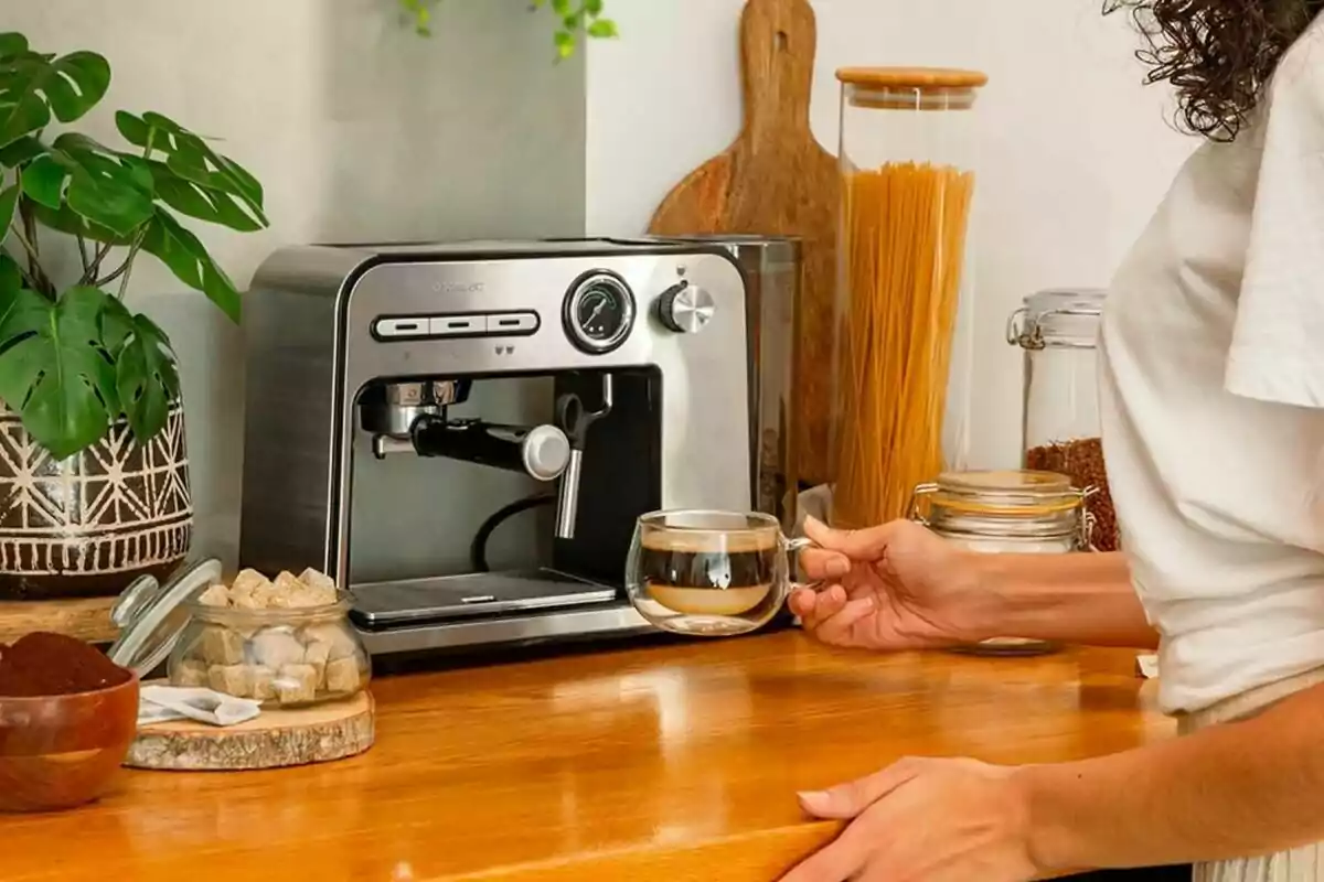 Persona preparando café con una máquina de espresso en una cocina, rodeada de plantas y frascos de ingredientes. Persona preparando café con una máquina de espresso en una cocina, rodeada de plantas y frascos de ingredientes.